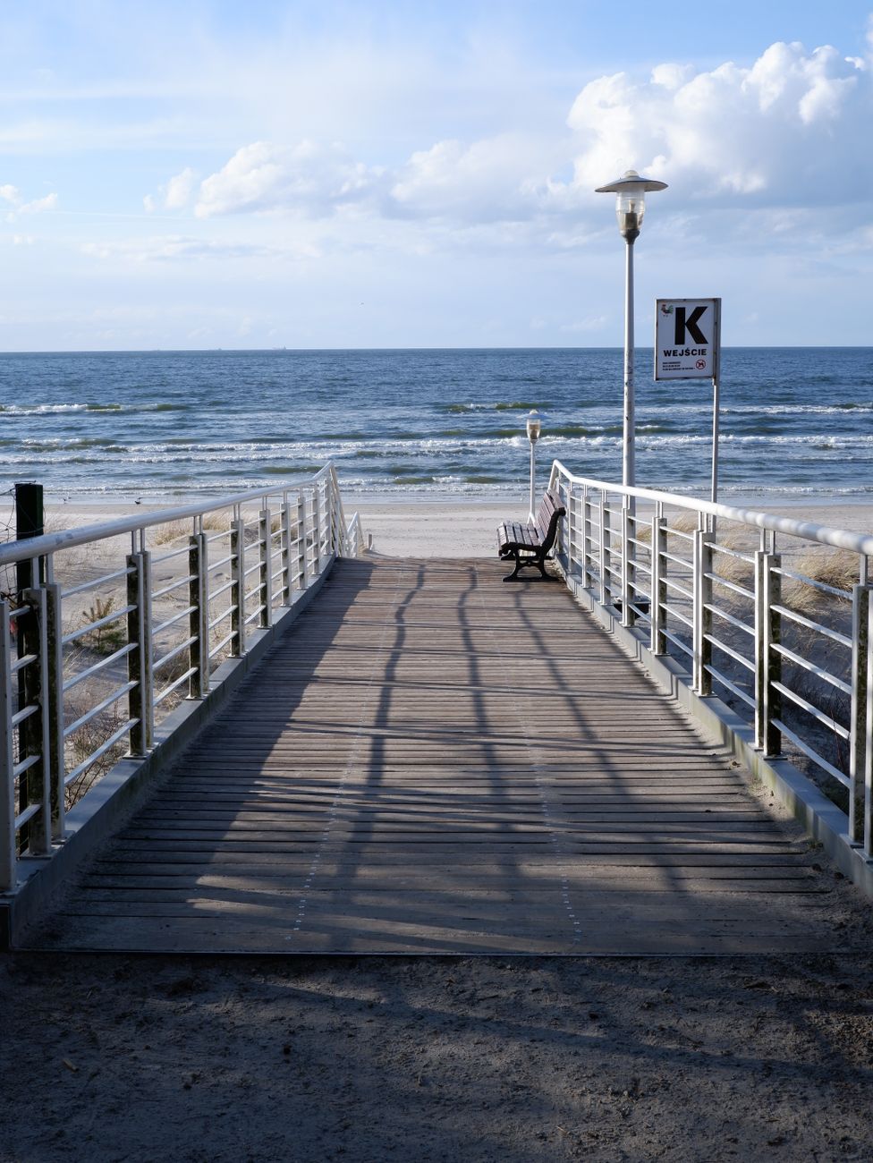 clouds over promenade with bench on beach