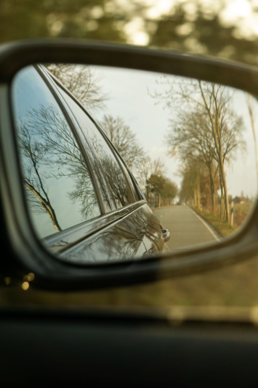 reflection of scenic tree lined road in car mirror