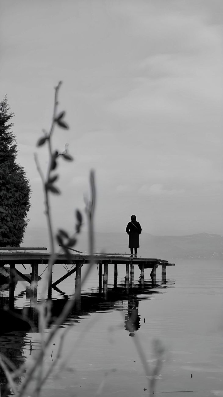 person stanidng on pier on lake under clouds