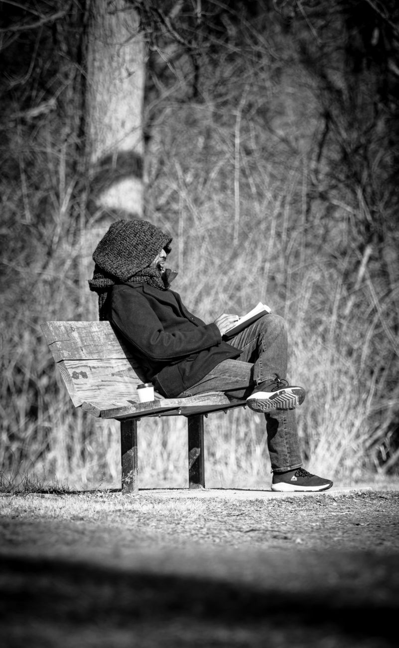 person in hood sitting on bench and reading