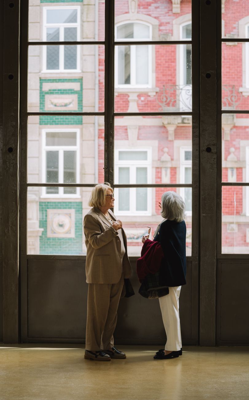 two elderly women looking at a building through a big window on the other side of the street