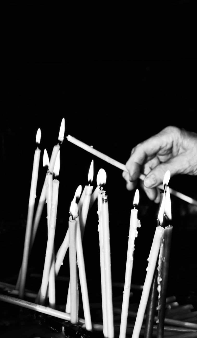 a grayscale photo of a person lighting a candle stick