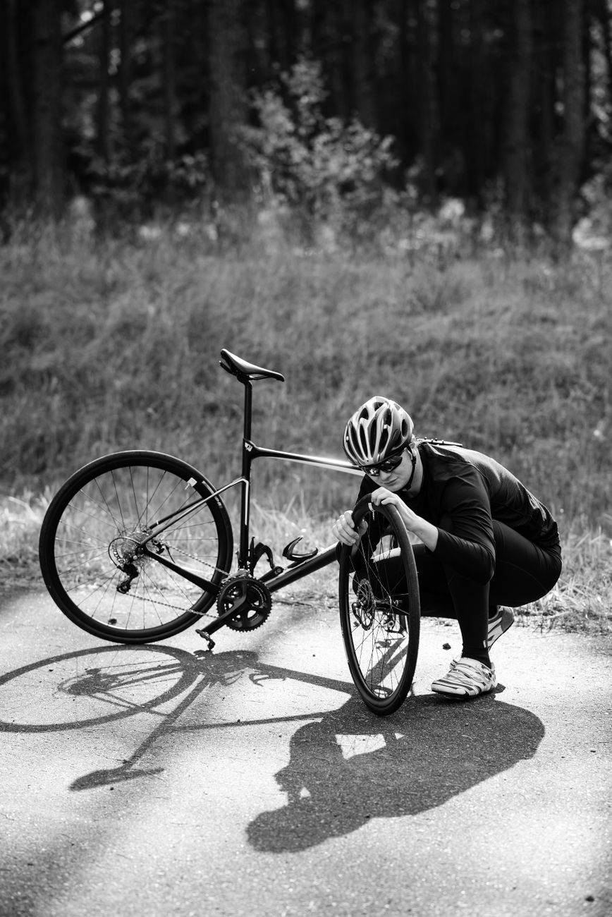 grayscale photo of a man repairing his bicycle on the street