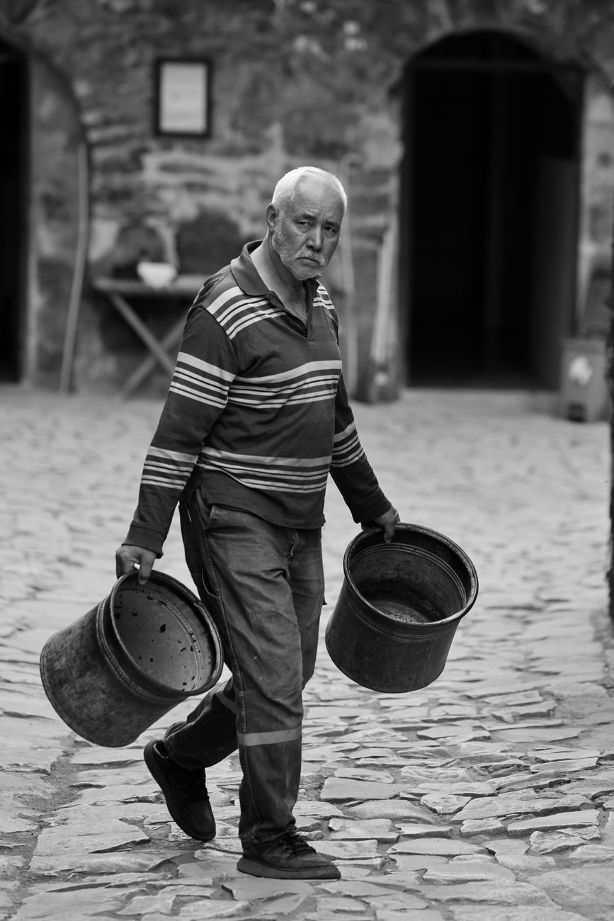 elderly craftsman carrying metal buckets outdoors