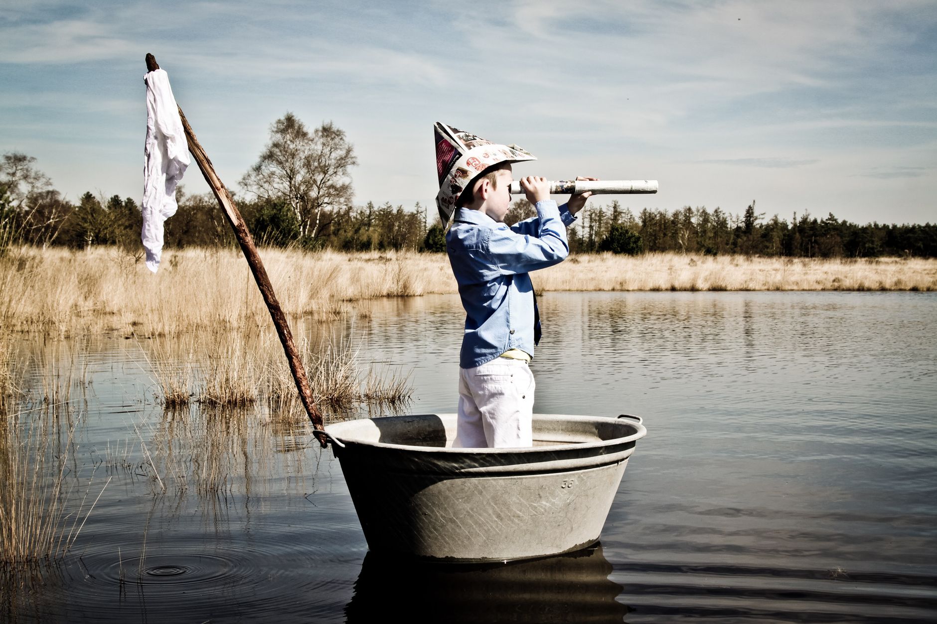 boy with paper hat looking through paper telescope at lake