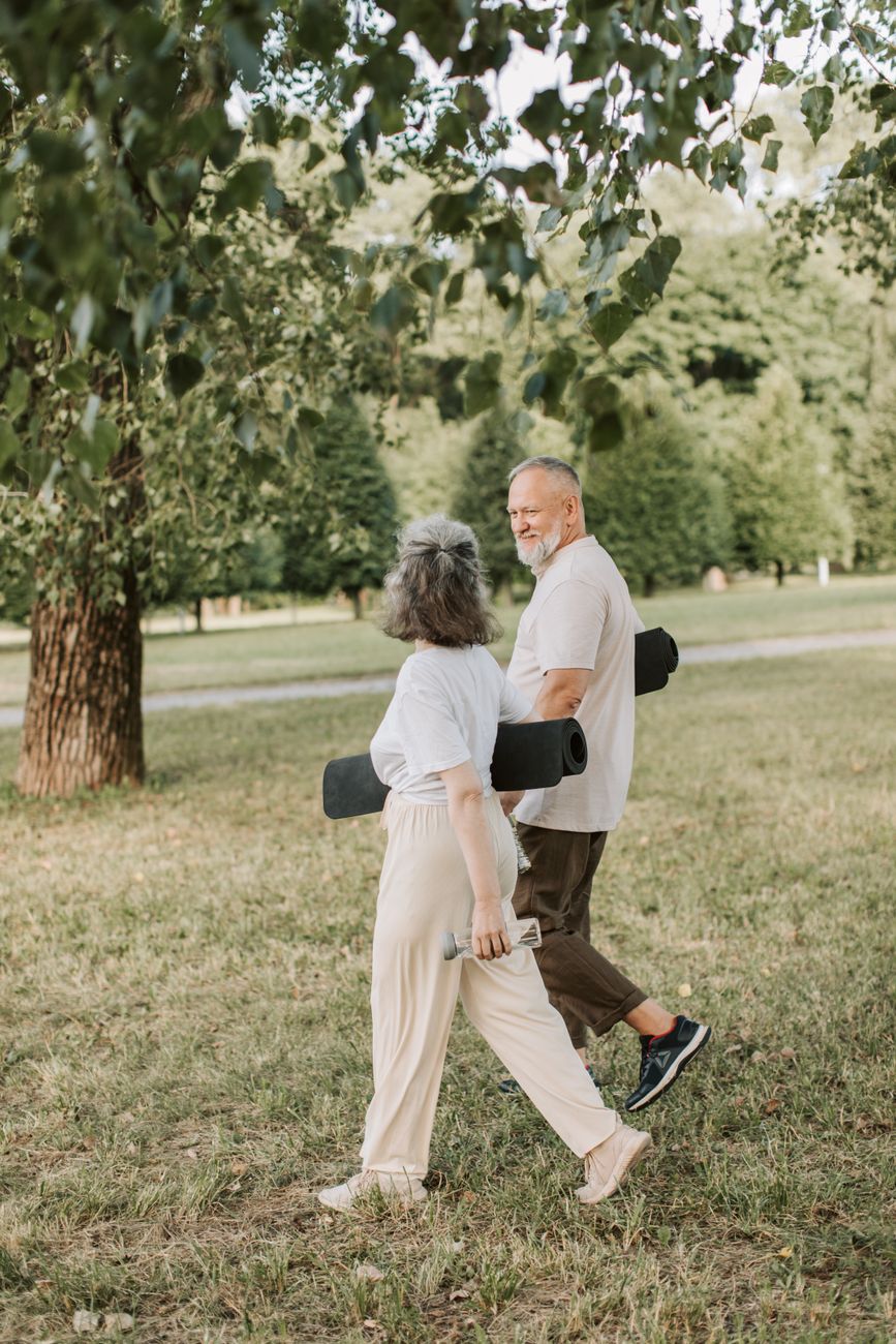 an elderly couple walking at the park while carrying yoga mat