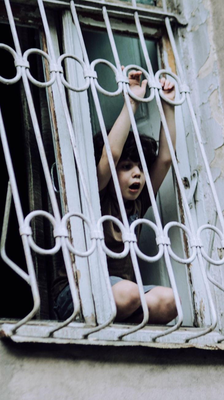 little kid playing on windowsill of weathered house