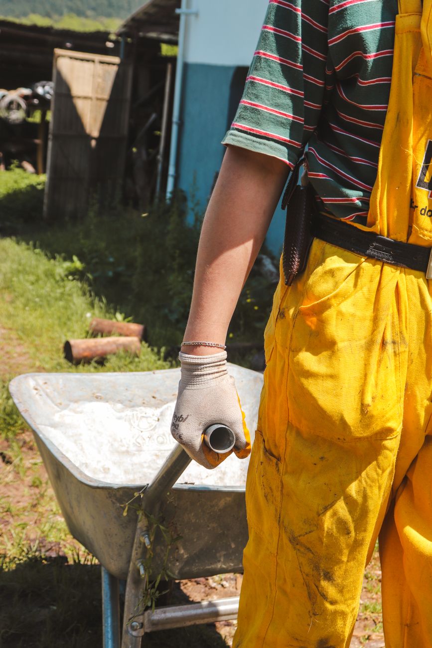 gardener in yellow overalls with wheelbarrow outdoors